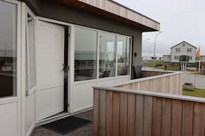 Un edificio moderno con grandes ventanales de vidrio, una terraza de madera y una puerta.