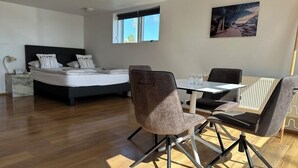 Een moderne hotelkamer met een bed, een eettafel met stoelen, een raam en een schilderij aan de muur.