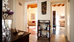 A room with a wooden desk, a vase with flowers, a bookshelf, and a patterned sofa. - VinsLounge B&B (Barletta)