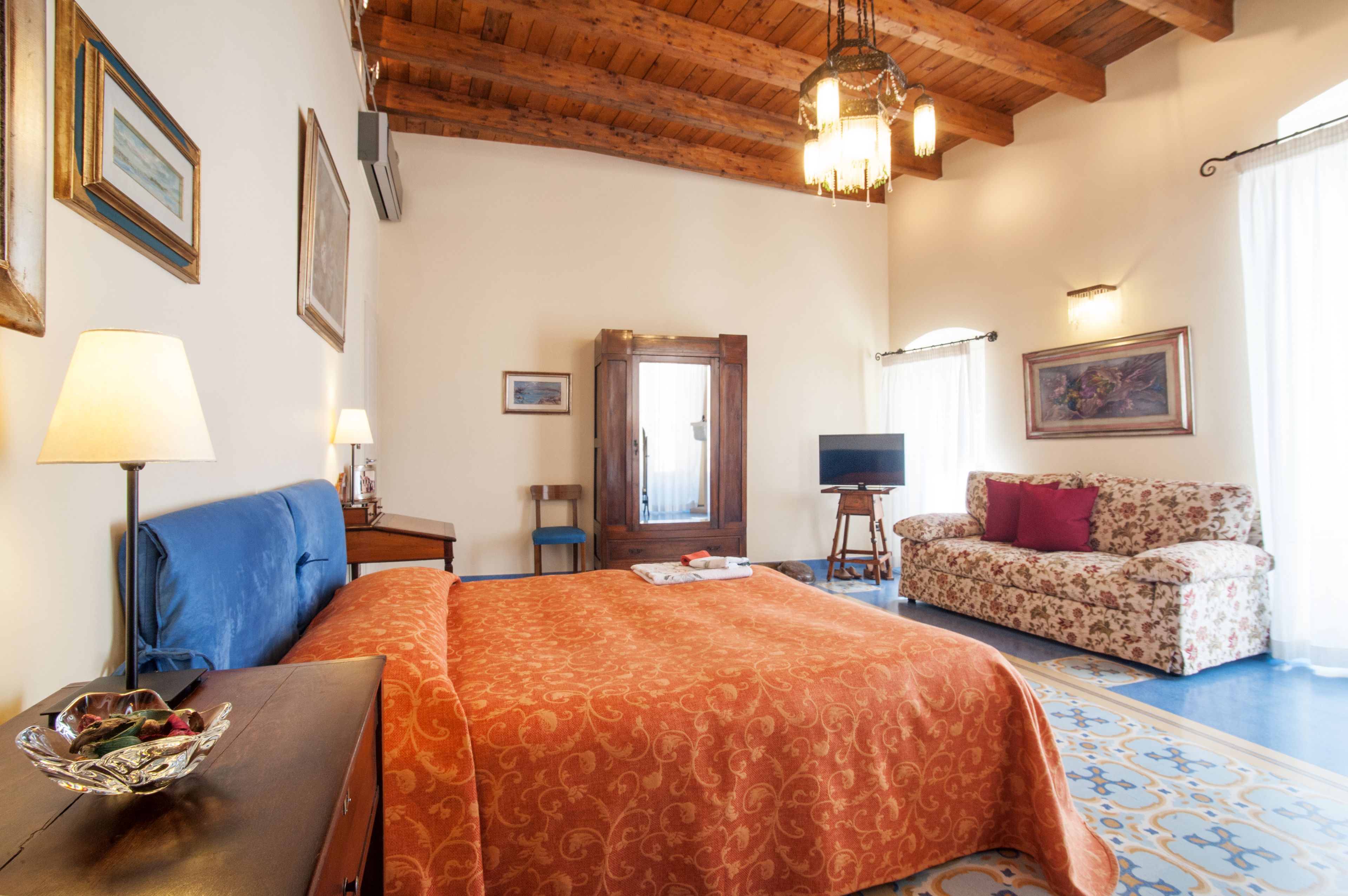 Une chambre d’hôtel avec un plafond en bois, un lit recouvert d’une courtepointe orange, un canapé, une télévision et un tableau accroché au mur.