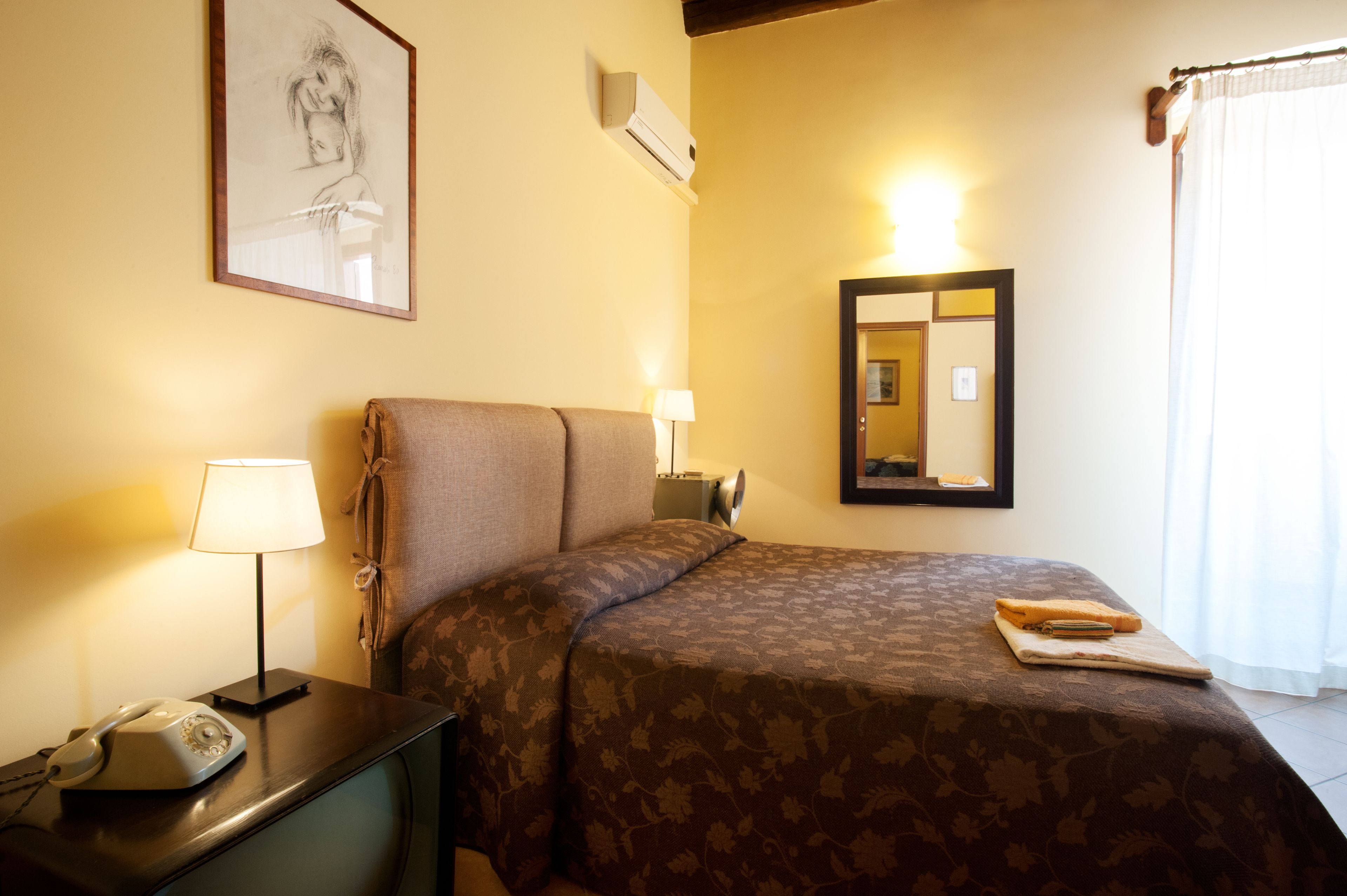 A hotel room with a bed, bedside lamp, telephone, and a framed artwork on the wall.