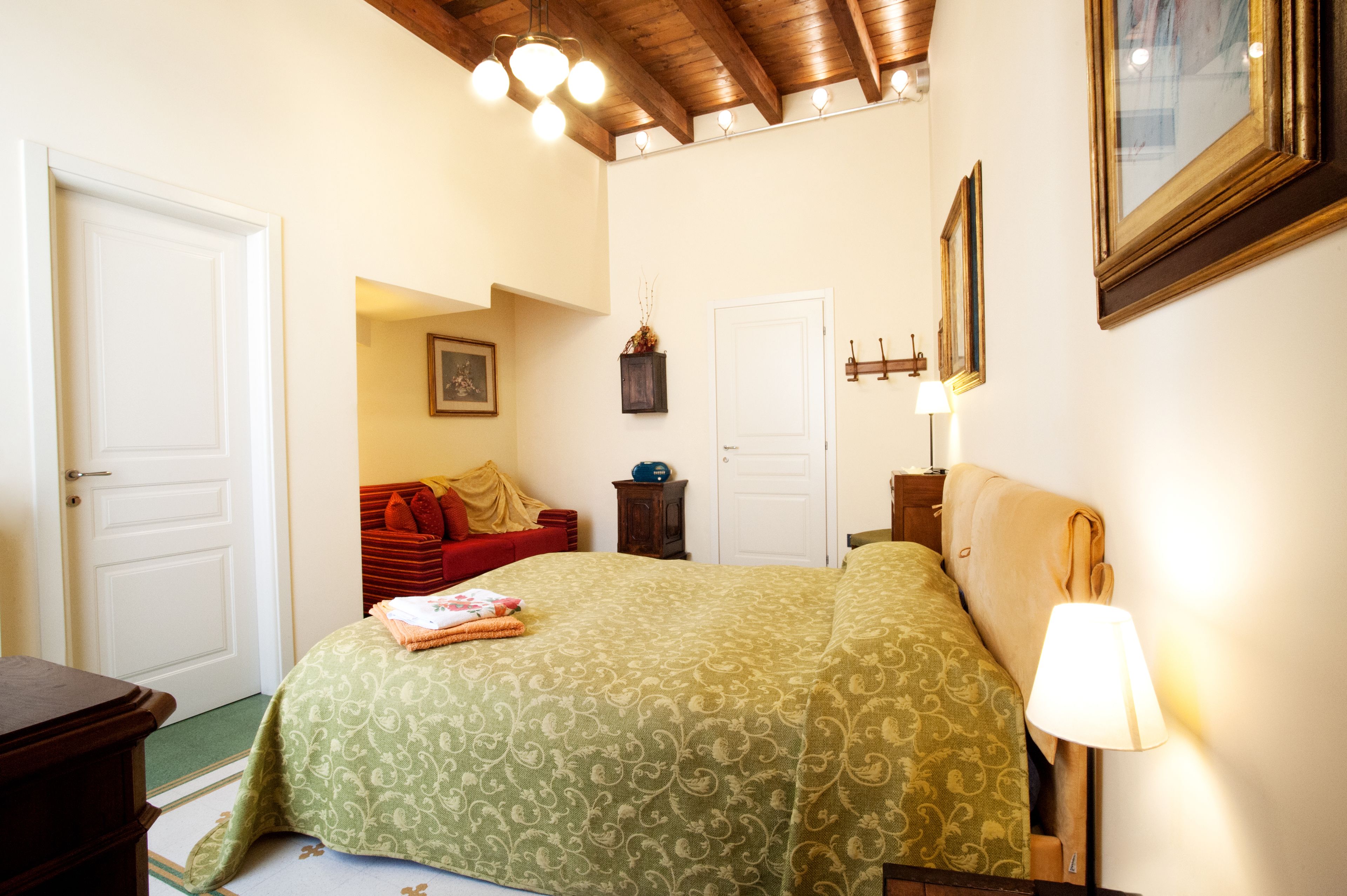 A bedroom with a bed, a nightstand, a lamp, a door, and a small cabinet.