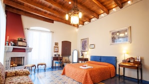 A hotel room with a wooden ceiling, a fireplace, a bed with an orange bedspread, a blue sofa, and a patterned rug. - VinsLounge B&B (Barletta)