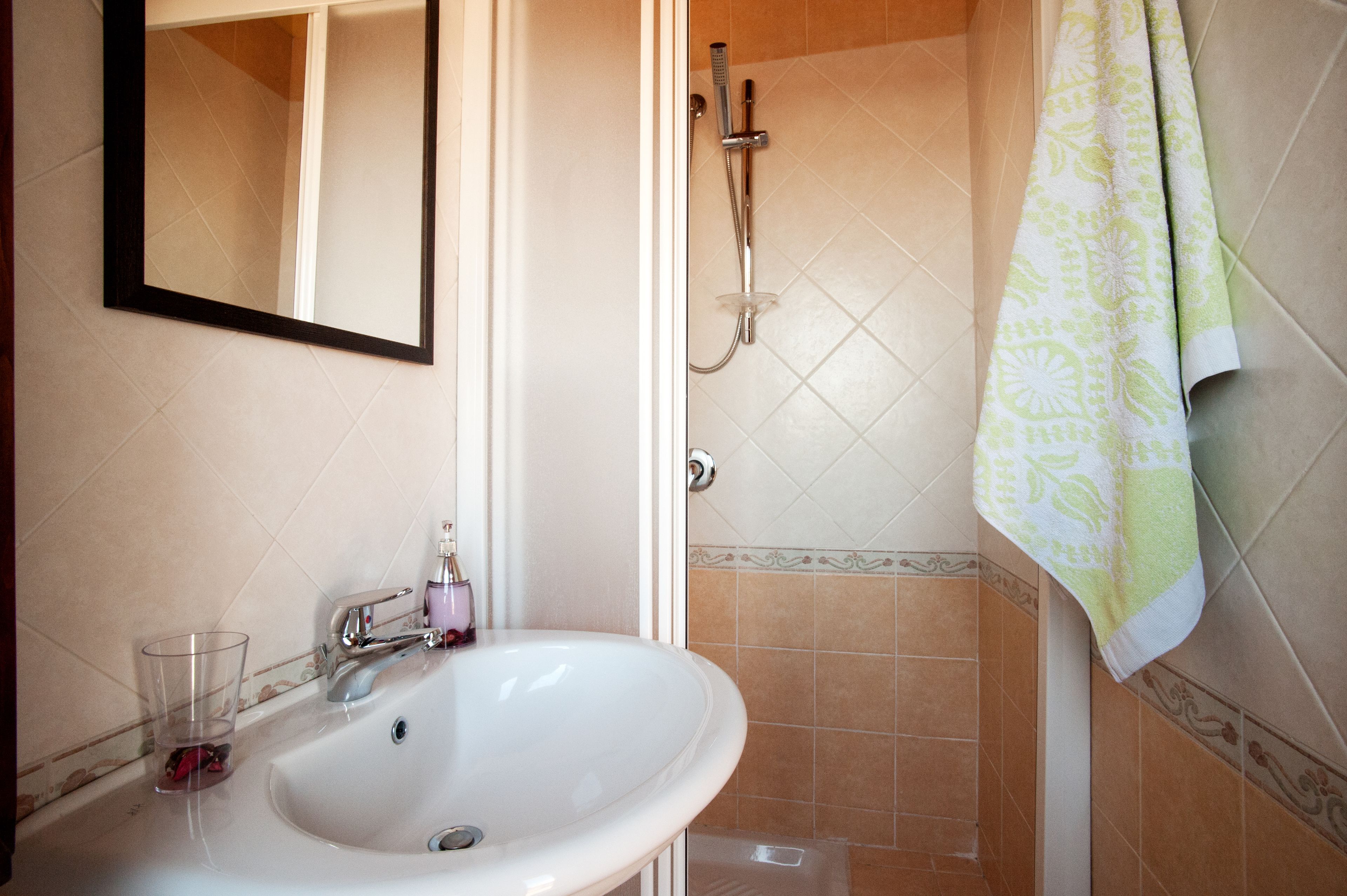 A bathroom with a sink, mirror, shower, and towel hanging on the wall.