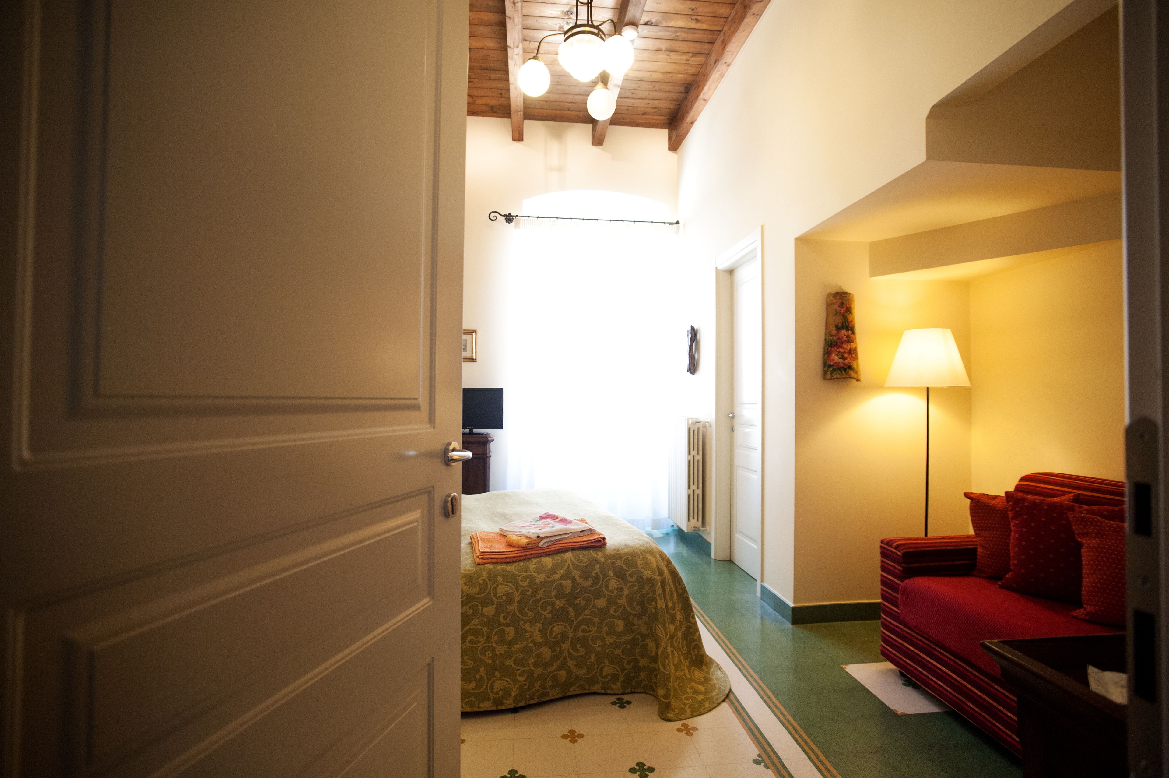 A room with a bed, a red sofa, a lamp, and a ceiling light fixture.
