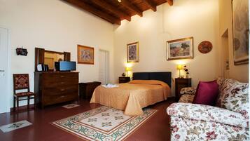 Un dormitorio con cama, cómoda, sillón, sofá, televisión y cuadros en las paredes.