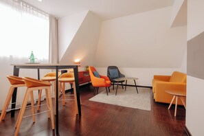 Un salon moderne avec un coin repas, comprenant une table en bois, des chaises orange, un canapé et une petite table d’appoint.