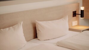 Een hotelkamer met een bed, kussens, een hoofdbord en een wandlamp.