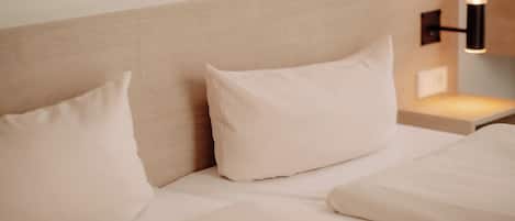 A hotel room with a bed, pillows, a headboard, and a wall-mounted light fixture.