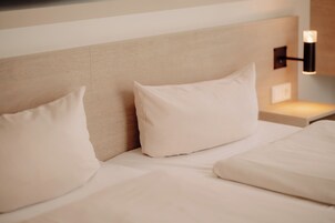 A hotel room with a bed, pillows, a headboard, and a wall-mounted light fixture.