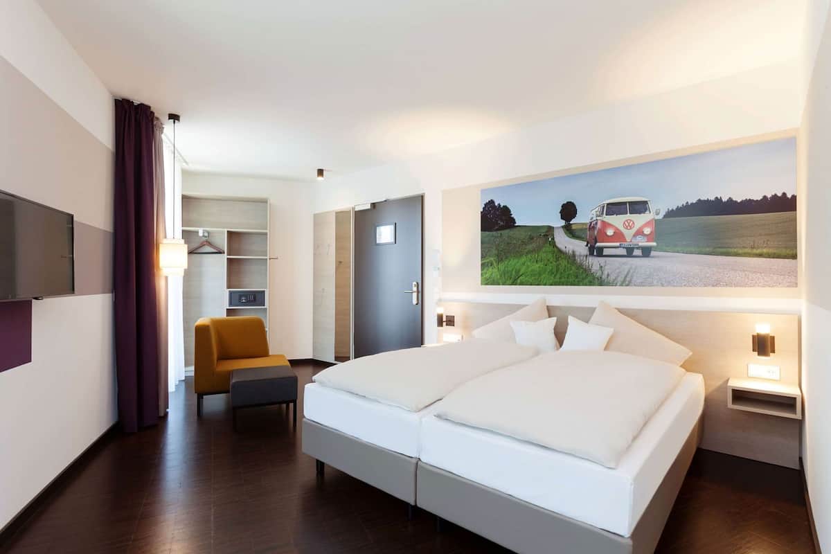 Una habitación de hotel con una cama grande, un escritorio, una silla, un televisor, una estantería y un cuadro en la pared.