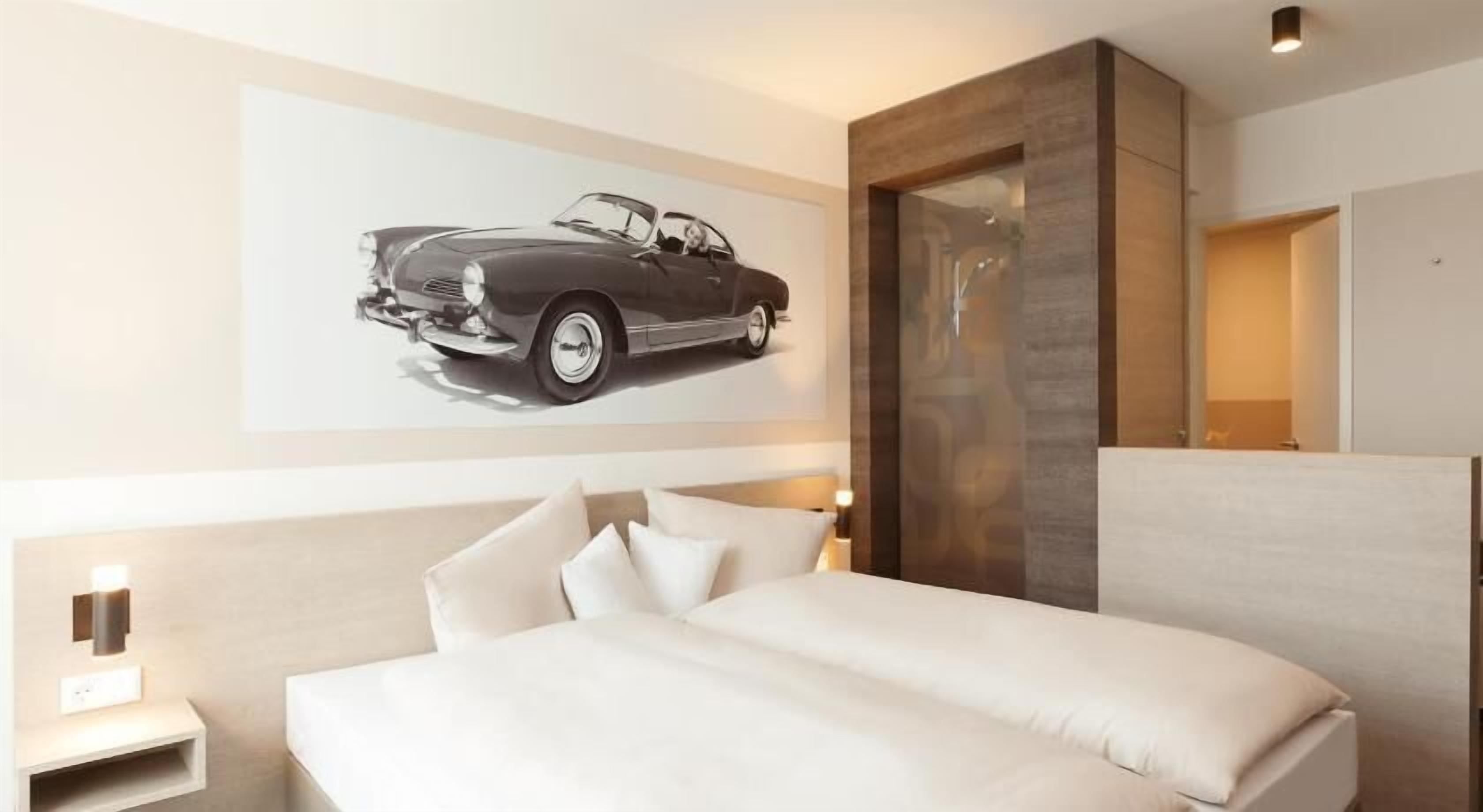 Une chambre d’hôtel moderne, dotée d’un grand lit, d’une table de chevet, d’une lampe fixée au mur et d’une grande fenêtre.