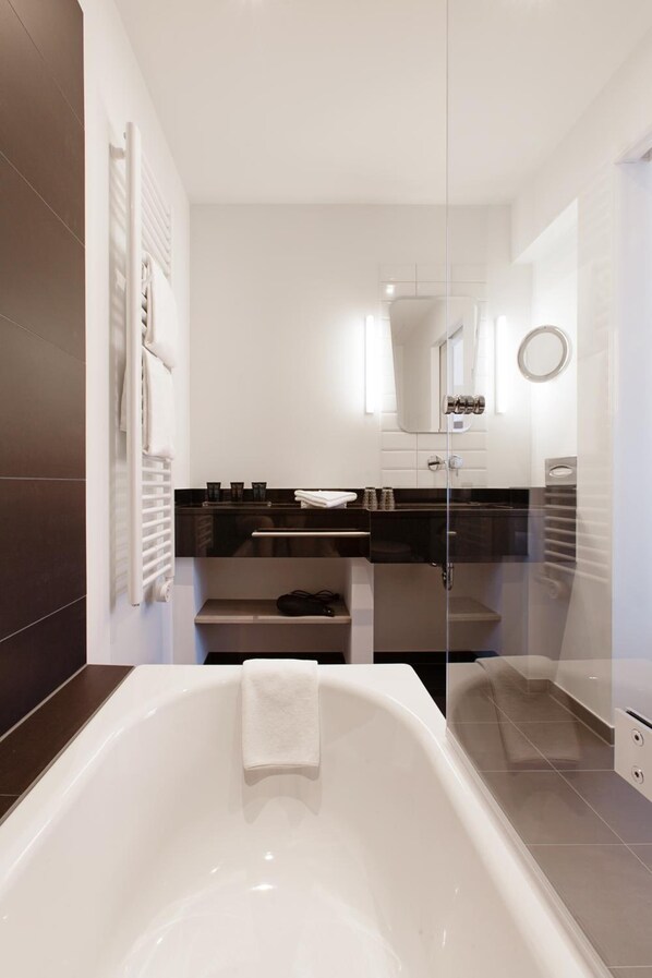 A modern bathroom with a bathtub, a glass shower enclosure, and a vanity with a mirror. - CROSS INN Osnabrück by Hackmann (Osnabrueck)