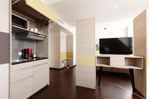 Een kleine keuken met een magnetron, koffiezetapparaat en een televisie op een standaard.