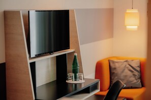Un espace de vie moderne avec un téléviseur à écran plat fixé sur un panneau en bois, une bouteille en verre et un verre posé sur un dessous de verre, le tout sur une surface noire.