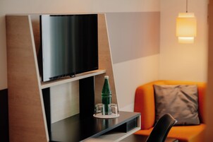 Un área de estar moderna con un televisor de pantalla plana montado en un panel de madera, una botella de vidrio y un vaso sobre un posavasos en una superficie negra.
