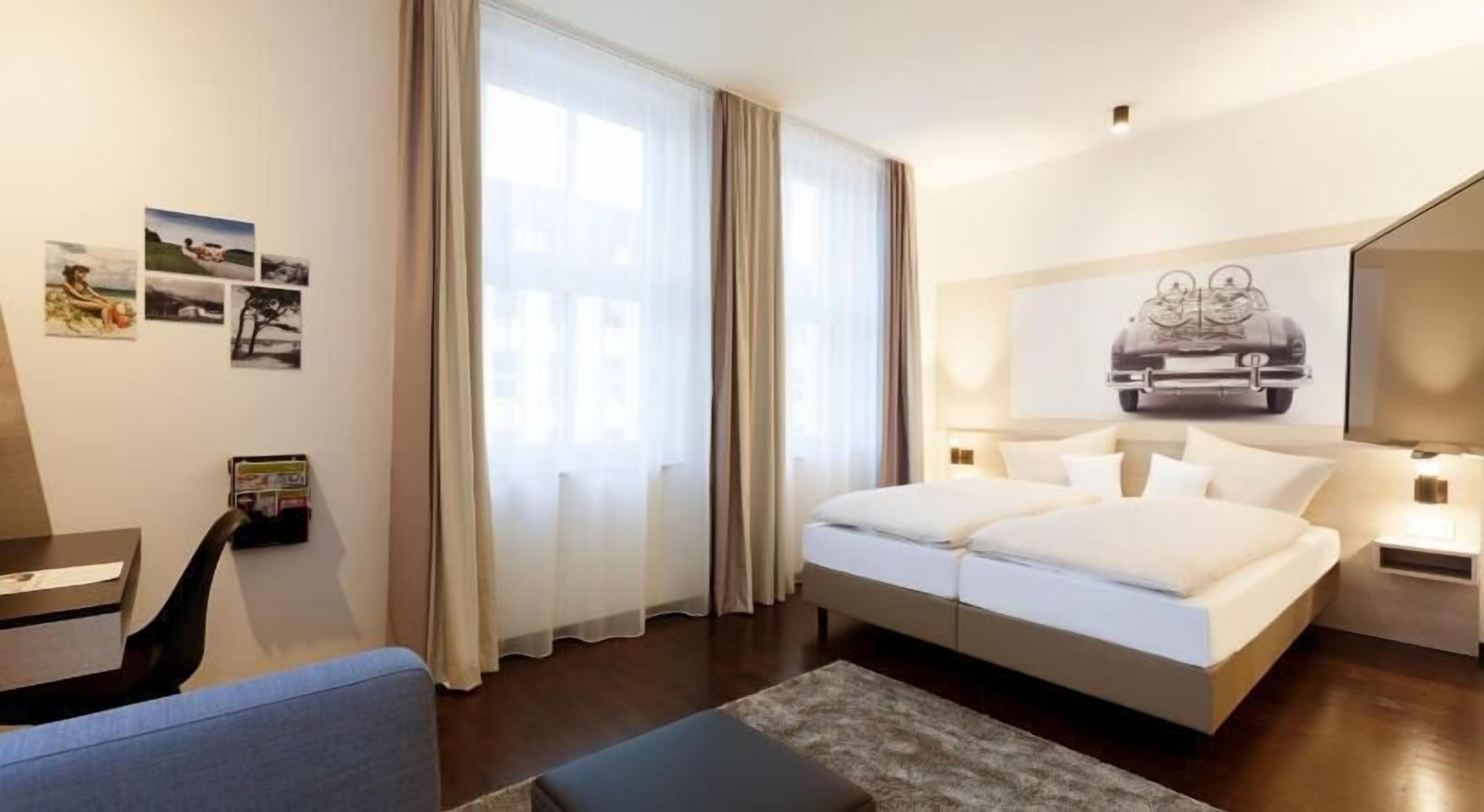 Une chambre d’hôtel avec un lit, un bureau, une chaise et une grande fenêtre avec des rideaux.