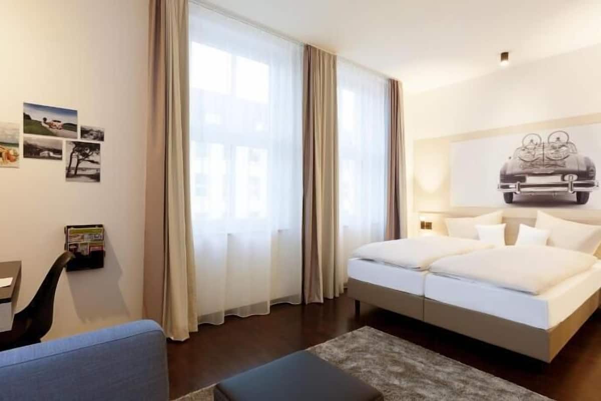 Hotellihuone, jossa on sänky, työpöytä, tuoli ja suuri ikkuna, jossa on verhot.
