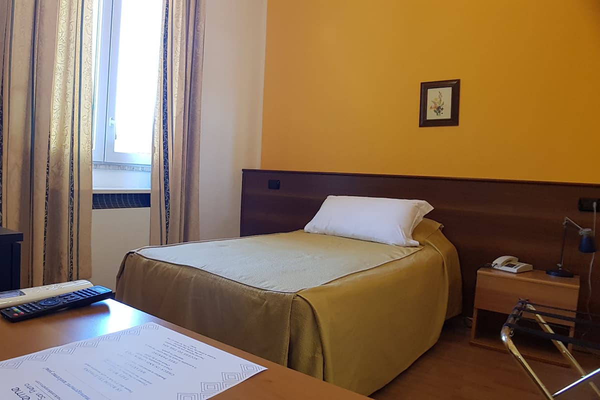 A hotel room with a bed, a desk with a TV, a remote control, and a lamp.