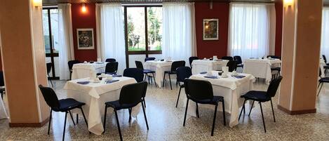 Comedor con mesas dispuestas, sillas y ventanas grandes con cortinas.