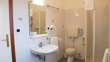 Un bagno con lavandino, WC e doccia bianchi. Sopra il lavandino c'è un portasciuga e a parete uno specchio.
