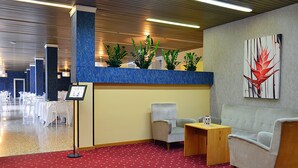 Un hall de hotel con alfombra roja, dos sillones, una mesita de madera y un arreglo de plantas en macetas.