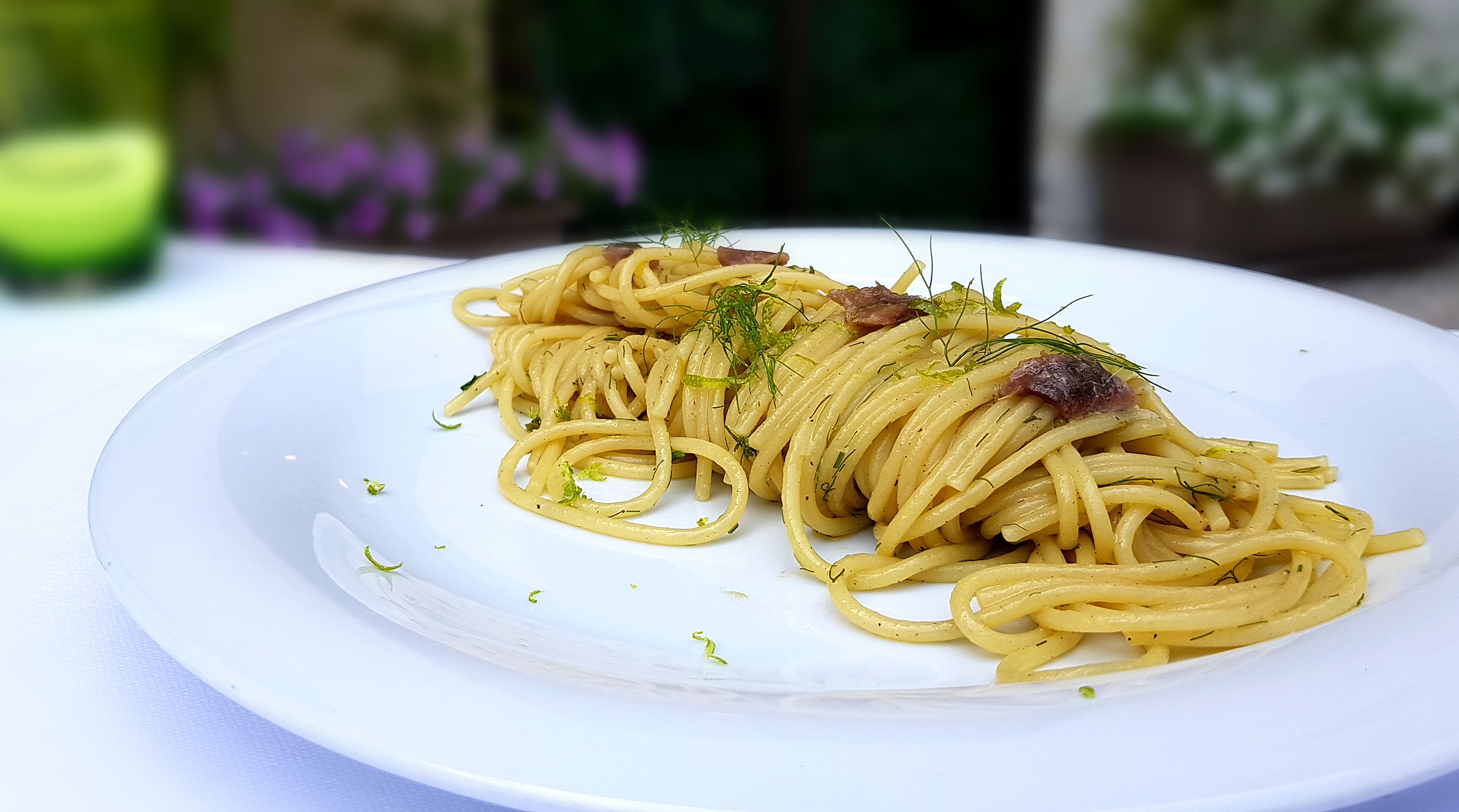 A plate of spaghetti with herbs and a garnish on a white plate.