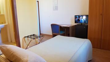 Hotelkamer met een bed, een bureau met stoel, een televisie, een klein kastje en een badkamer met wastafel en spiegel.