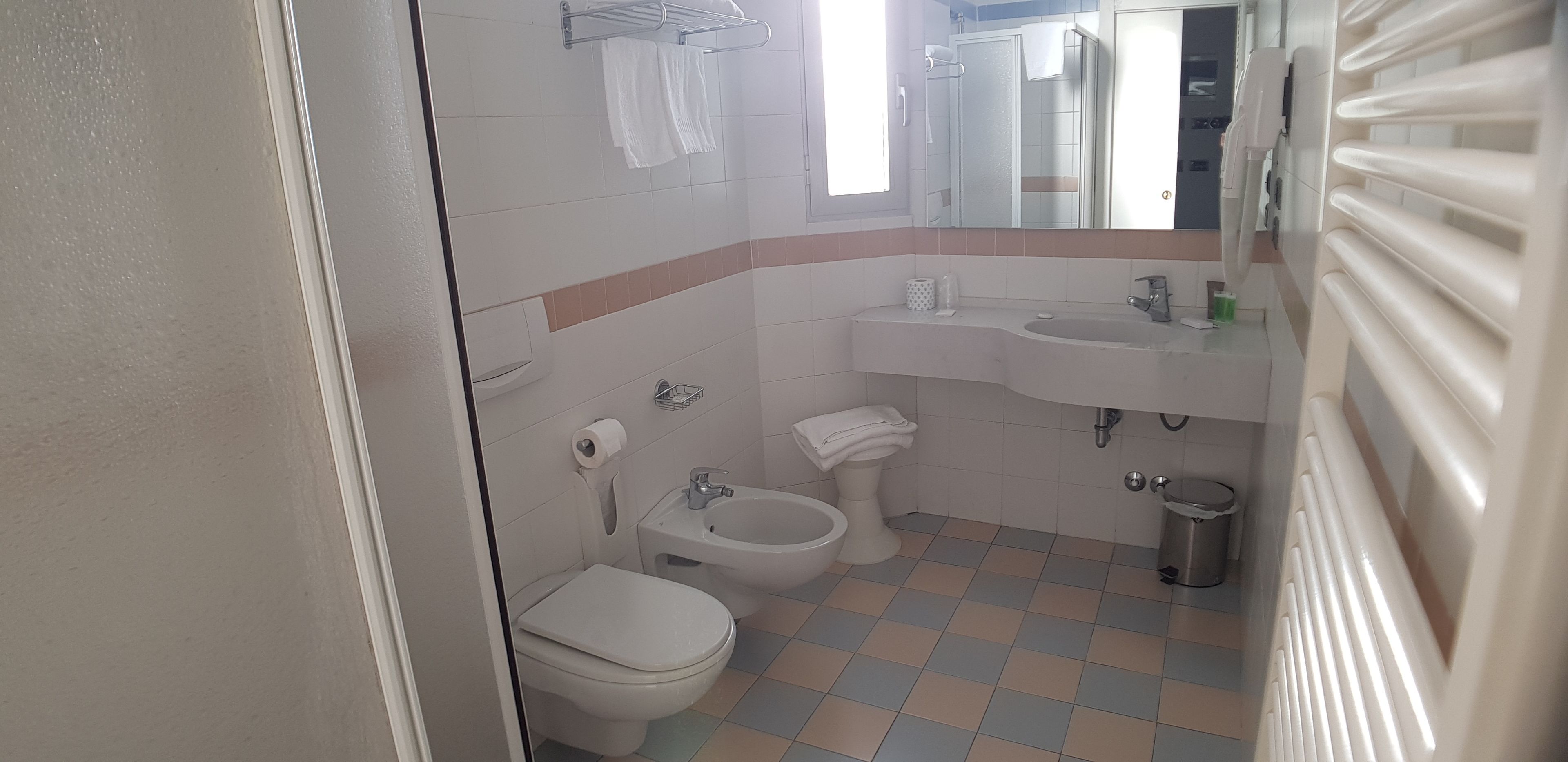 Un baño con inodoro, bidé, lavamanos y espejo.