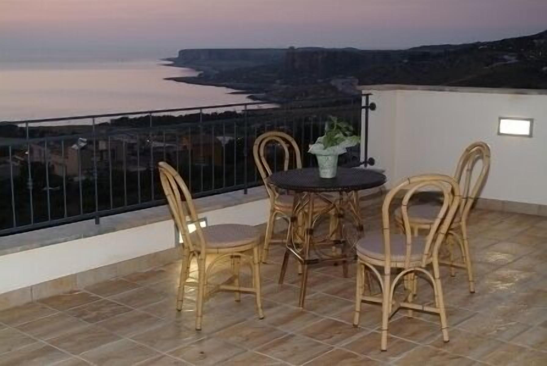 Un balcón con sillas de mimbre y una mesa, con vistas a un paisaje costero.