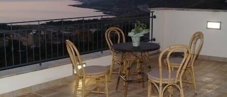 Un balcón con sillas de mimbre y una mesa, con vistas a un paisaje costero.