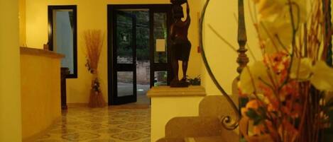 A hallway with patterned flooring, a reception desk, a statue, and a door leading outside.