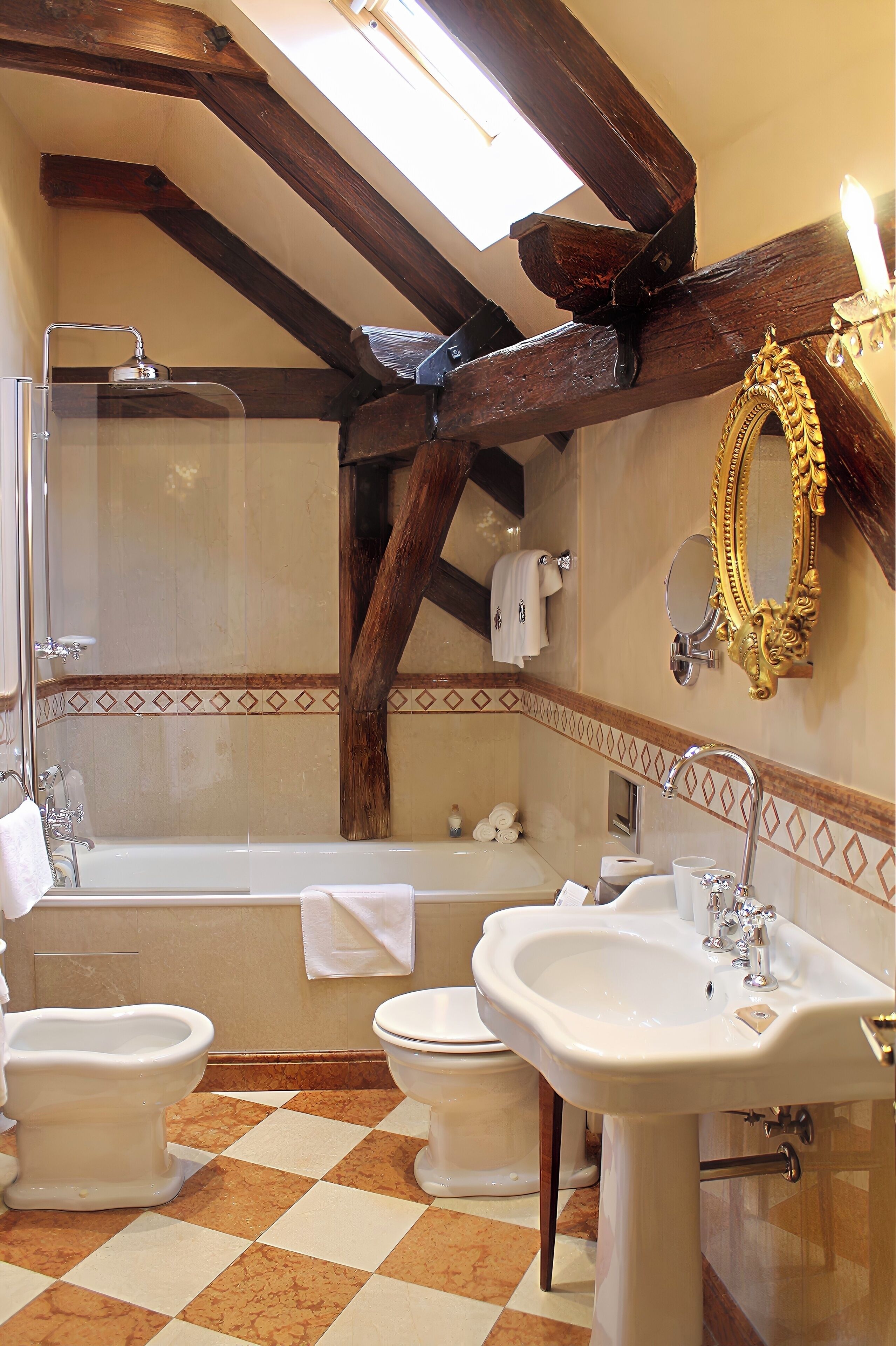 A bathroom with a checkered floor, a bathtub, two toilets, a sink, and a mirror with an ornate frame.