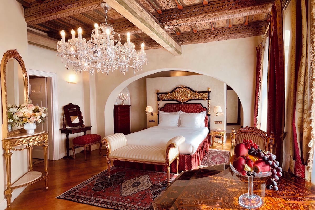 A luxurious bedroom with a large bed, ornate chandelier, and a red and gold color scheme.