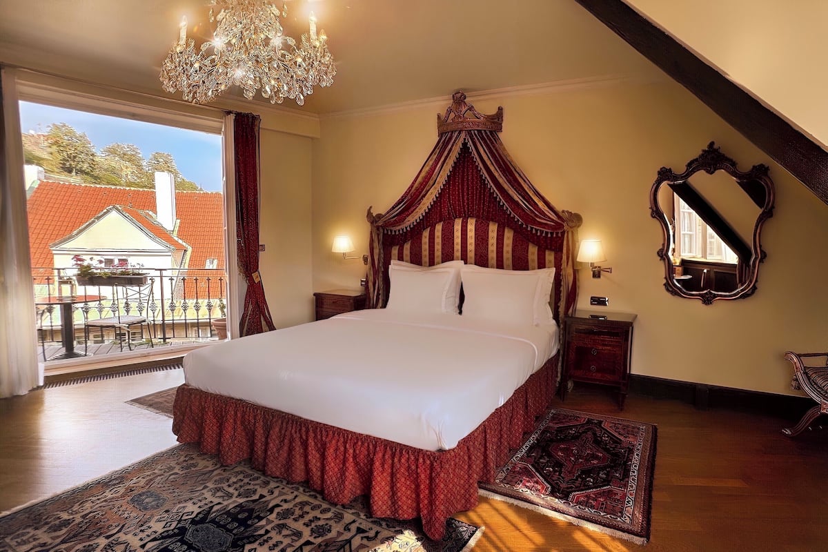A bedroom with a large bed, a chandelier, a mirror, and a view of a building through a window.