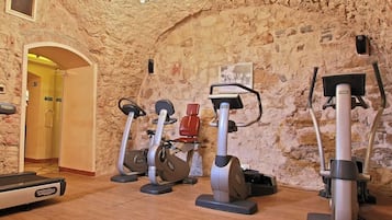 A gym with various exercise equipment, a wooden floor, and a stone wall.