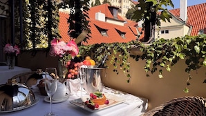 An outdoor dining area with a table set for two, featuring a dessert plate, wine glasses, and a fruit basket. - Alchymist Prague Castle Suites Hotel (Prague)