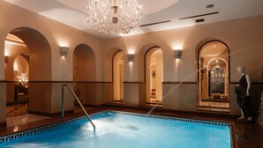 A luxurious indoor swimming pool with a geometric tile border, arched doorways, and a chandelier. - Alchymist Prague Castle Suites Hotel (Prague)