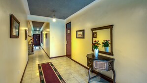 A hallway with a tiled floor, a red and green rug, a wooden console table with a vase of flowers, and a mirror. - The Milimani Lodge (Arusha)