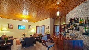 A bar area with a wooden ceiling and stone wall, featuring a bar counter and shelves with bottles. - The Milimani Lodge (Arusha)