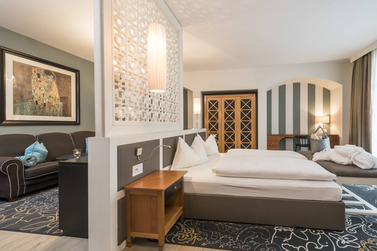 Une chambre d’hôtel avec un grand lit, un bureau, une chaise, un canapé et un élément décoratif mural.