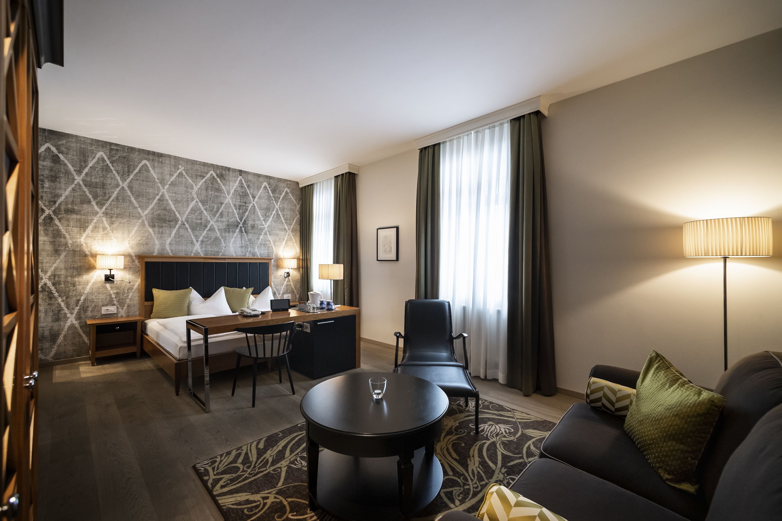 A hotel room with a bed, desk, two chairs, a sofa, and a lamp.