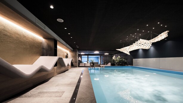 An indoor swimming pool with a wavy seating area and a modern ceiling design.