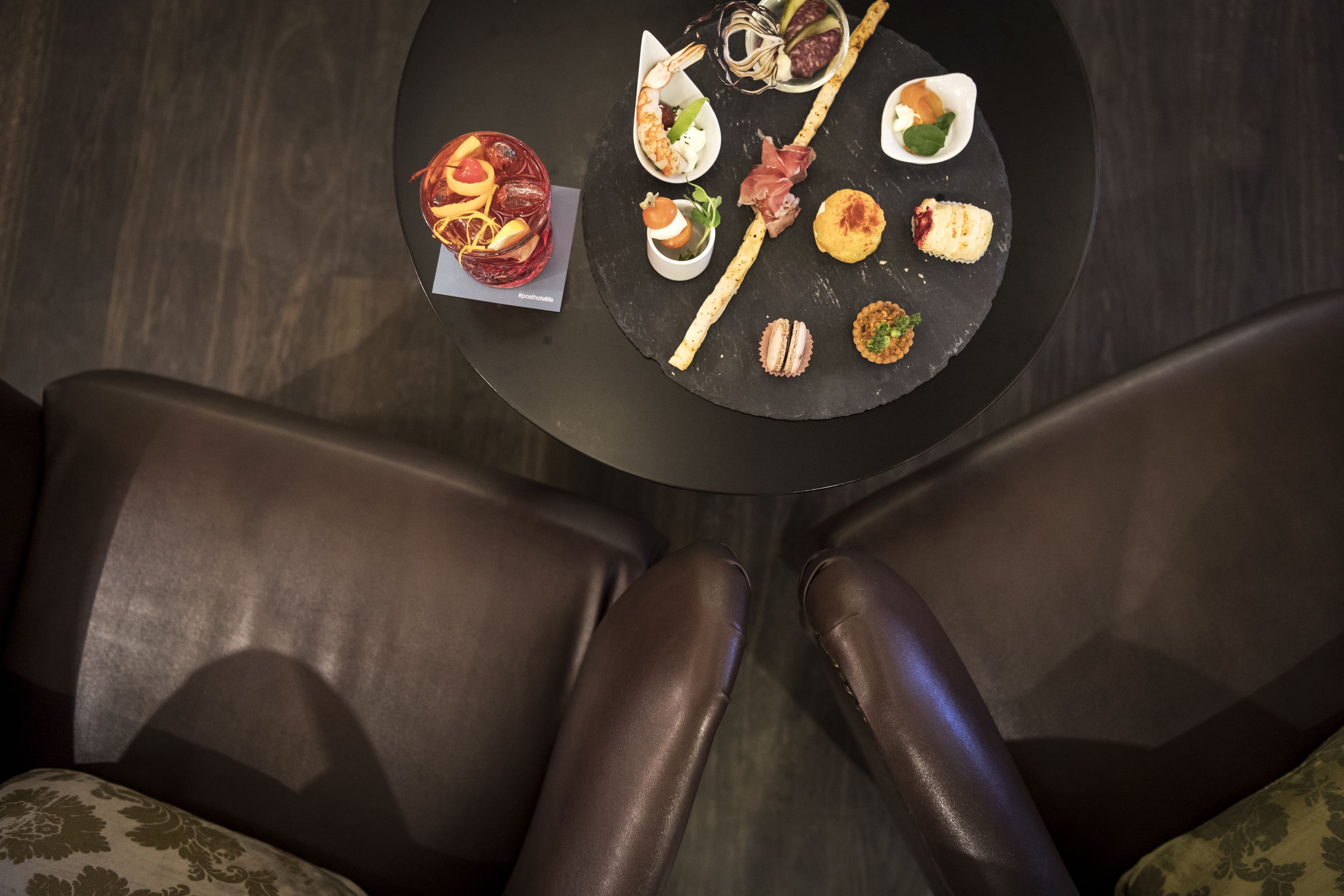 Una mesa redonda con diversos alimentos, como mariscos, verduras y pasteles, rodeada de sillas de cuero marrón oscuro.