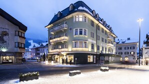 A multi-story hotel with balconies, a snow-covered street, and illuminated windows. - Post Hotel - Adults Only (San Candido)