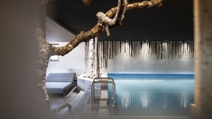 An indoor swimming pool with a glass barrier, a white bench, and a decorative tree branch. - Post Hotel - Adults Only (San Candido)