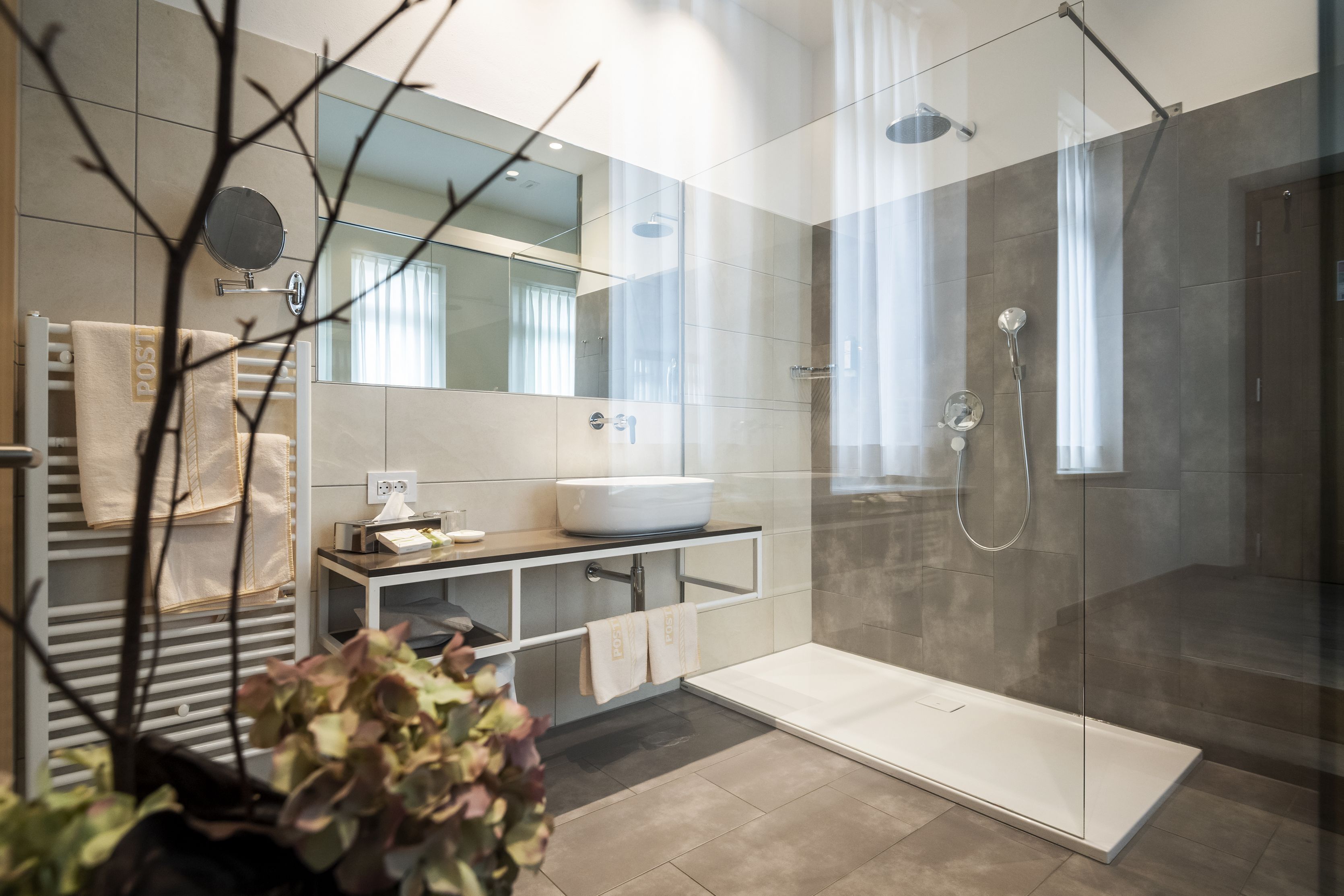 Un baño moderno con ducha de vidrio, lavabo blanco y un espejo grande.