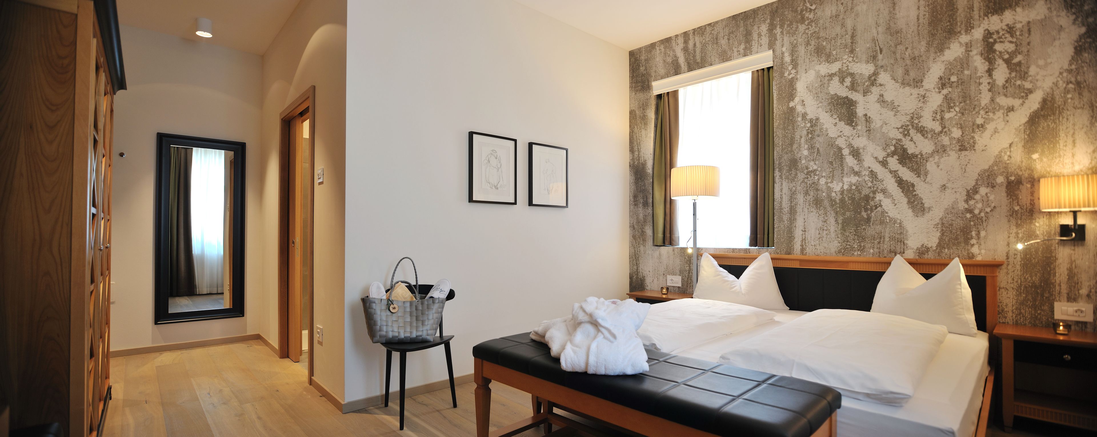 Une chambre d’hôtel avec un grand lit, une banquette, une chaise, un bureau et une fenêtre avec des rideaux.