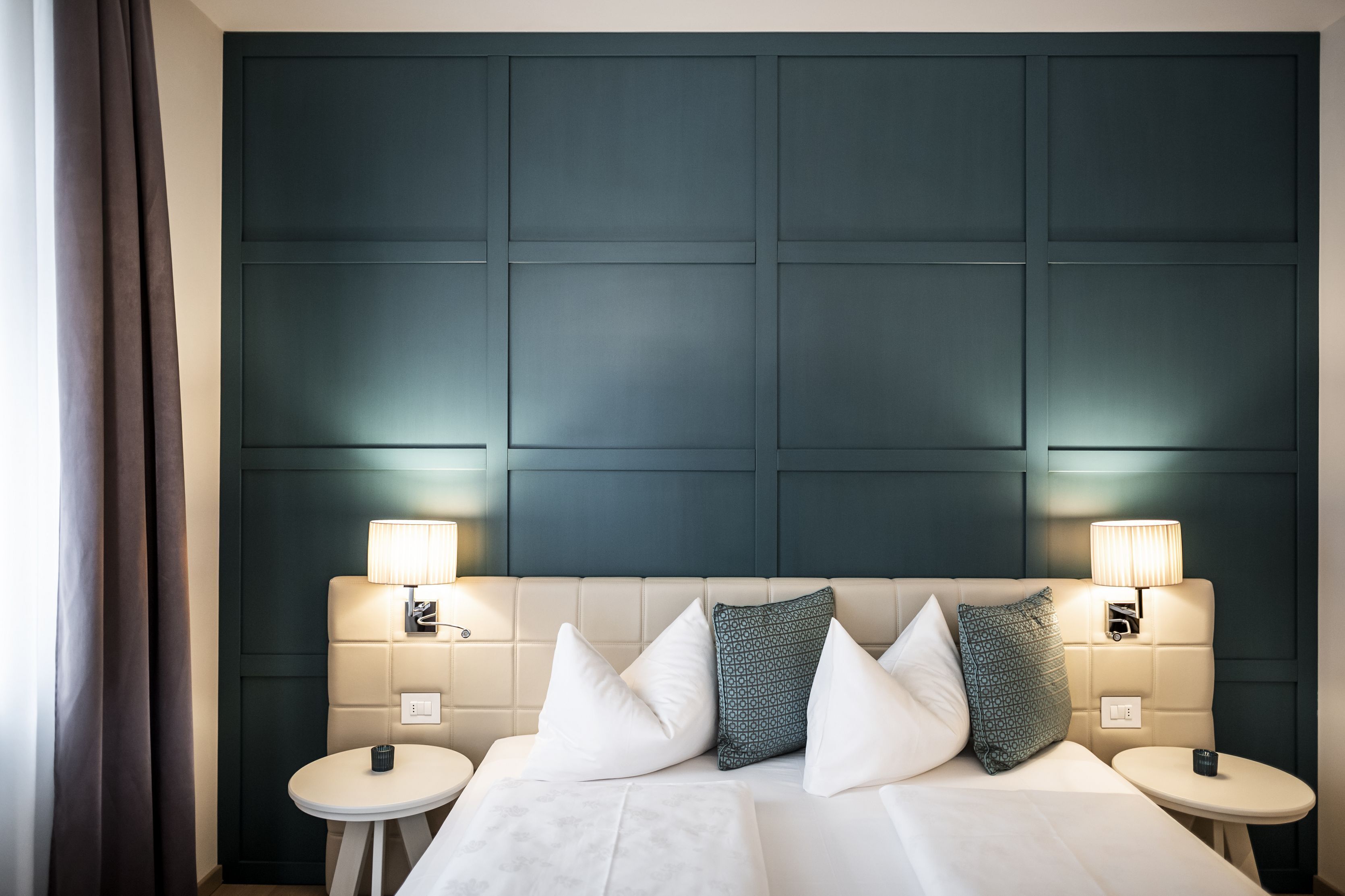 Ein Hotelzimmer mit einem großen Bett, zwei Nachttischen, einem Kopfteil mit integrierter Beleuchtung und dunkel gefärbeter Wandverkleidung.