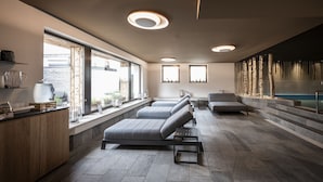 A modern spa room with a large window, a seating area, and a stone wall with a water feature.